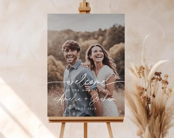 May include: Welcome sign for a wedding with a photo of the couple in front of a forest background. The sign says "Welcome to the wedding of Amelia + Graham 06.21.2028".