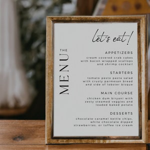 Op de afbeelding: Een ingelijst menu met de tekst "let's eat!" en een lijst met voorgerechten, soepen, hoofdgerechten en desserts. Het menu is getiteld "The Menu" en is geschreven in een eenvoudig, modern lettertype.