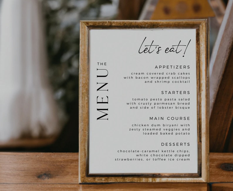 Op de afbeelding: Een ingelijst menu met de tekst "let's eat!" en een lijst met voorgerechten, soepen, hoofdgerechten en desserts. Het menu is getiteld "The Menu" en is geschreven in een eenvoudig, modern lettertype.