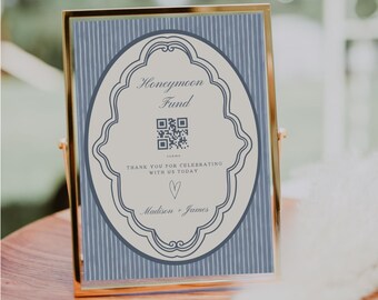 May include: A gold-framed sign with a blue and white striped background. The sign features an oval design with the words "Honeymoon Fund" and a QR code. The text "Thank you for celebrating with us today" and names "Madison + James" are also included.
