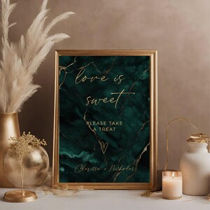May include: A gold framed sign with a green marble background. The text on the sign reads "love is sweet" in gold script. Below the text is "Please take a treat" and a small gold heart. The bottom of the sign reads "Clarissa + Nicholas".