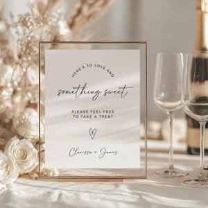 Könnte beinhalten: Ein klares Acrylschild mit goldenem Rahmen, auf dem der Text "HERE'S TO LOVE AND something sweet PLEASE FEEL FREE TO TAKE A TREAT ♡ Clarissa + James" steht.
