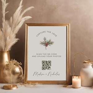 Może przedstawiać: Złoty znak z białym tłem i zieloną gałązką sosny z czerwonymi jagodami. Znak zawiera napis "Capture the Love" oraz kod QR z tekstem "Scan the QR code and upload your photos" i "Madison + Nicholas".
