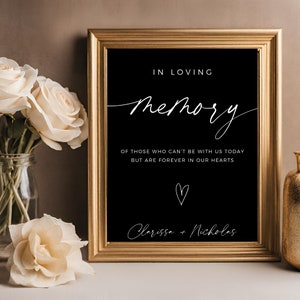 May include: A black framed sign with white text that reads "In loving memory of those who can't be with us today but are forever in our hearts." A heart symbol is below the text, followed by the names "Clarissa + Nicholas".