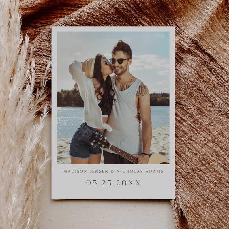 May include: A photo booth style wedding announcement with a photo of a couple kissing on a beach. The text reads "MADISON JENSEN & NICHOLAS ADAMS 05.25.20XX".