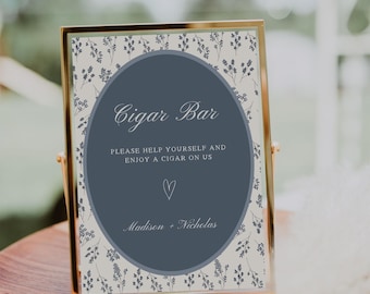 May include: A gold-framed sign with the text "Cigar Bar" in elegant script. The sign has a blue oval in the center with the text "PLEASE HELP YOURSELF AND ENJOY A CIGAR ON US" and a heart symbol. The background features a floral pattern.