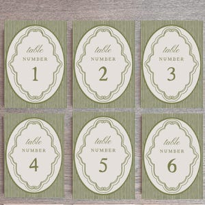 May include: Set of six table number cards. Each card features a cream-colored oval with the words "table NUMBER" and a number from 1 to 6 in a serif font. The background is a light green striped pattern.