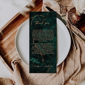 Puede incluir: Una tarjeta de agradecimiento de boda con un diseño de mármol verde oscuro y letras doradas. La tarjeta incluye el texto "thank you" y un mensaje sincero. La tarjeta está colocada en un plato blanco con cubiertos dorados.