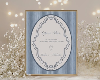 May include: A framed sign with a gold border features the text "Open Bar" in elegant script. The sign has a blue and white striped background with an oval-shaped central design. The text "SIP SIP HOORAY THE DRINKS ARE ON US TODAY!" is also included.