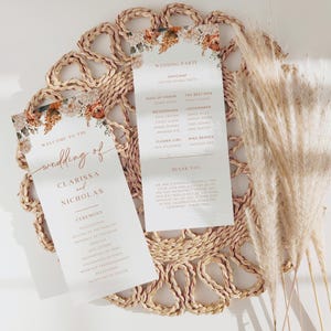 May include: Wedding ceremony programs with floral accents, featuring the names Clarissa and Nicholas. The programs are on a woven placemat with pampas grass. The text includes wedding party details and a thank you message.