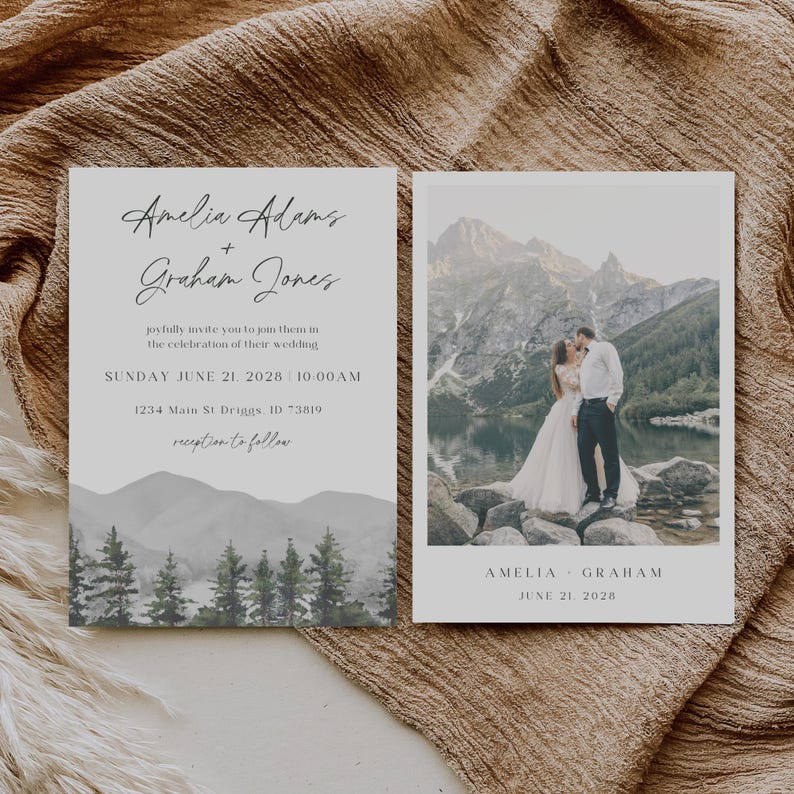 May include: Wedding invitation with a watercolor mountain landscape and a photo of a couple kissing in front of a lake. The text on the invitation reads "Amelia Adams + Graham Jones" and "Sunday June 21, 2028, 10:00 AM".