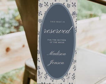 May include: A rectangular wedding seat reservation sign with a floral pattern background. The sign has a dark blue oval in the center with the word "reserved" in cursive. Below it reads "FOR THE MOTHER OF THE BRIDE" and the names "Madison Jensen".