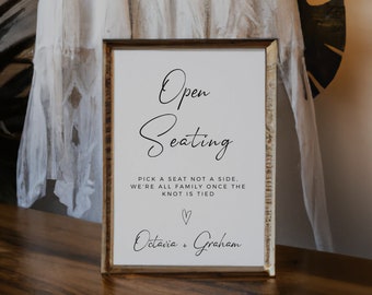 May include: A white sign in a gold frame with black text that reads "Open Seating" and "Pick a seat not a side. We're all family once the knot is tied."  A heart symbol and the names "Octavia + Graham" are also included.