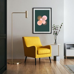 Puede incluir: Un sillón amarillo con una impresión abstracta rosa y marrón enmarcada en verde oscuro encima. Una lámpara de pie dorada y una pequeña mesa auxiliar con un jarrón de flores rosas también están en la imagen.