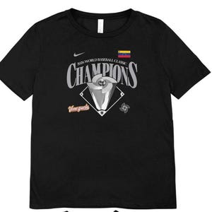 Op de afbeelding: Zwart T-shirt met de tekst "2026 World Baseball Classic Champions". Het ontwerp bevat een honkbaltrofee, de Venezolaanse vlag en het woord "Venezuela". Een Nike-logo is zichtbaar.