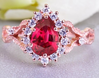May include: A rose gold ring featuring a vibrant, pear-cut red gemstone, encircled by smaller, clear stones. The band has delicate detailing and further small stones. The ring is displayed on a soft, neutral surface, with floral accents in the background.
