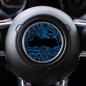 May include: A black leather steering wheel with a blue and black patterned design in the center.