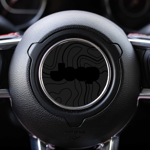 May include: Black leather steering wheel with a black and gray Jeep logo on a topographic map design.