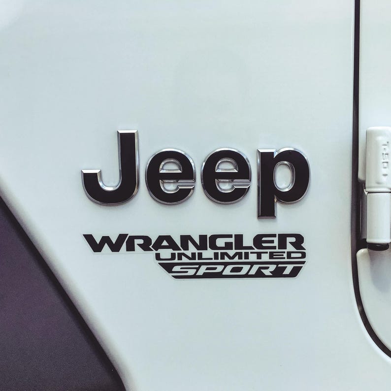 May include: Close-up of a white vehicle panel with the black and chrome Jeep logo and the words "WRANGLER UNLIMITED SPORT" in black lettering. The vehicle's door hinge is visible on the right side.