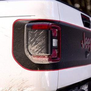 May include: A white Jeep with a red and black stripe design. The rear taillight is visible and has a red and black design. The Jeep has a black and white textured design on the side.