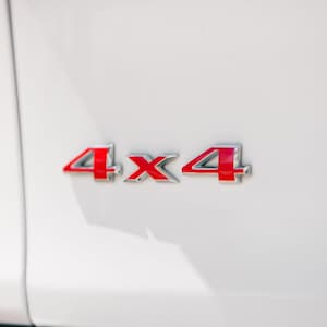 May include: Close-up of a white vehicle's body with a red and silver 4x4 emblem. The emblem is positioned on the side of the vehicle, with the numbers and letters in a bold, eye-catching design.