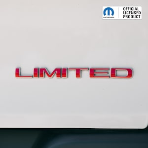 Peut inclure: Un emblème "LIMITED" rouge et chromé est affiché sur une surface blanche. L'emblème est en gras, avec une police sans empattement. Le coin supérieur droit présente le logo Mopar et le texte "OFFICIAL LICENSED PRODUCT."