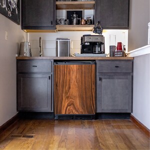 May include: A dark wood-paneled kitchen with a stainless steel refrigerator, a coffee maker, and dark gray cabinets. The cabinets have black handles and the refrigerator has a wood-grain finish.