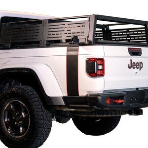 K&ouml;nnte beinhalten: Ein wei&szlig;er Jeep-Truck mit einem schwarzen Metall-Ladepritschenaufsatz. Der Truck hat schwarze und rote Streifen an der Seite und das Wort "Jeep" in roten Buchstaben auf der R&uuml;ckseite.