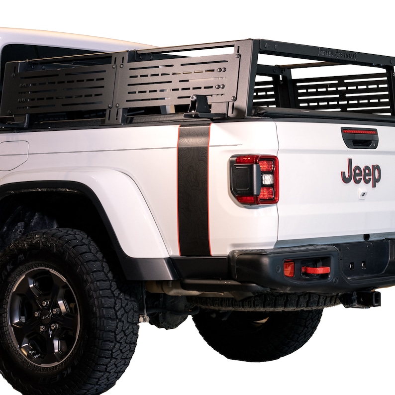 K&ouml;nnte beinhalten: Ein wei&szlig;er Jeep-Truck mit einem schwarzen Metall-Ladepritschenaufsatz. Der Truck hat schwarze und rote Streifen an der Seite und das Wort "Jeep" in roten Buchstaben auf der R&uuml;ckseite.