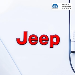 May include: A close-up of a white surface with the red word "Jeep" in a bold font. The upper right corner features the Mopar logo and the text "OFFICIAL LICENSED PRODUCT".