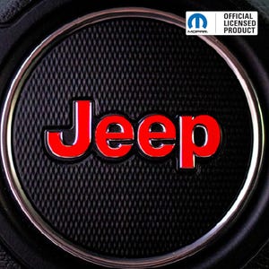 Może przedstawiać: Zbliżenie czarnej, teksturowanej odznaki z czerwonym słowem "Jeep" w srebrnym obrysie. Odznaka jest okrągła i ma srebrną obwódkę. W prawym górnym rogu znajduje się biały prostokąt z napisem "OFFICIAL LICENSED PRODUCT" i logo Mopar.