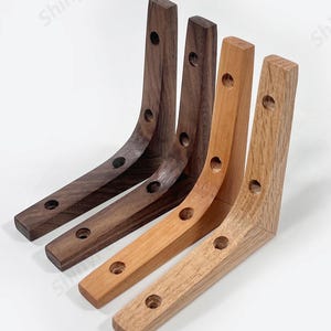 Puede incluir: Cuatro soportes de estantería de madera en diferentes tonos de madera. Dos son de nogal marrón oscuro, uno es marrón claro y uno es marrón medio. Cada soporte tiene cuatro agujeros para montaje.