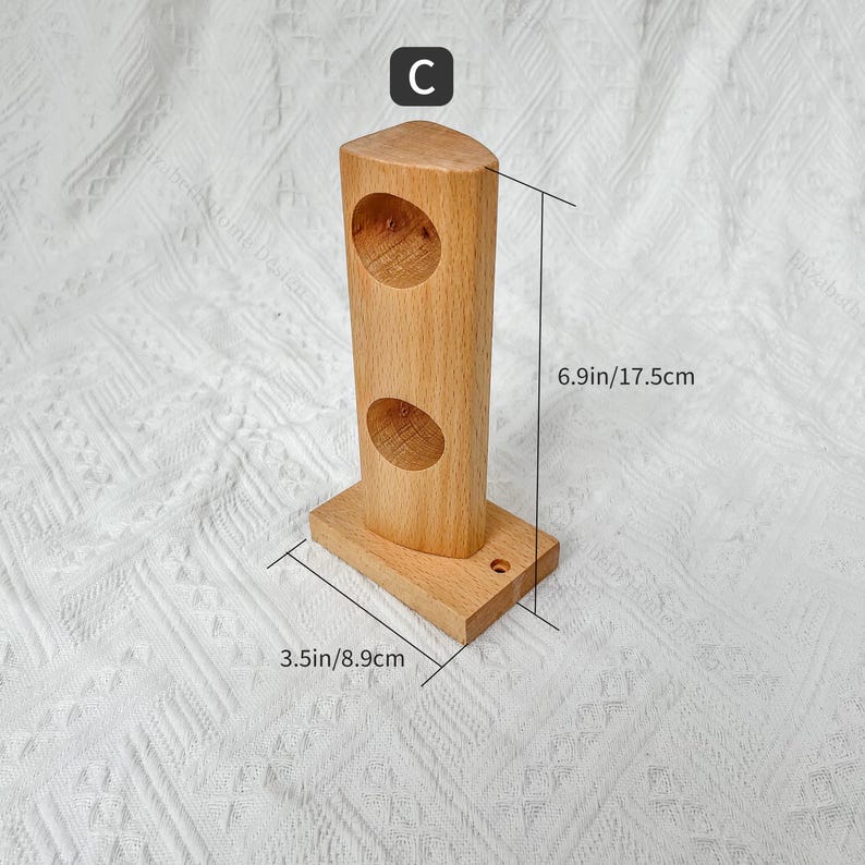 May include: Wooden wall mount with two round holes, measuring 17.5 cm tall and 8.9 cm wide. The mount is made of light brown wood and has a simple design.