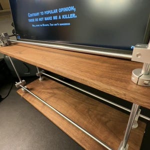 May include: A wooden shelf with two tiers, supported by metal rods and clamps. The shelf is made of dark wood with a natural grain pattern. A black television screen is mounted above the shelf, displaying the text "CONTRARY TO POPULAR OPINION, THESE DO NOT MAKE ME A KILLER."
