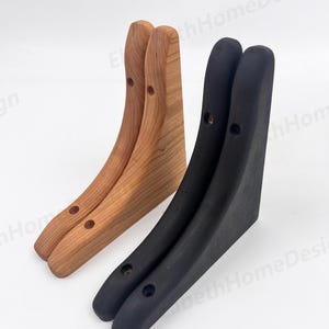 May include: Two sets of shelf brackets, one set is made of natural wood and the other is black. The brackets are curved and have two holes for mounting.