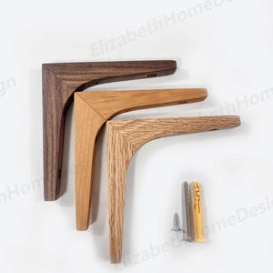 Könnte beinhalten: Drei Holz-Regalbretter in verschiedenen Holztönen: Dunkelbraun, Hellbraun und Naturholz. Die Halterungen sind L-förmig und haben eine leichte Krümmung. Zwei silberne Schrauben und ein gelber Kunststoffdübel sind im Lieferumfang enthalten.