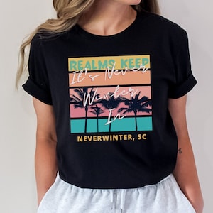 May include: Black t-shirt with a graphic print of palm trees and the text "Realms Keep It's Never Winter In Neverwinter, SC".