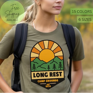 May include: A green t-shirt with a retro-style graphic of a sunset over mountains and trees. The graphic says "Long Rest Camp Grounds est 1974".