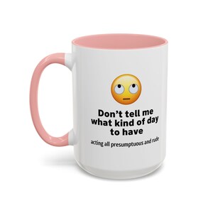 以下が含まれることがあります： ピンクの縁取りが付いた白いセラミック製のコーヒーカップ。カップには、混乱した表情の黄色い絵文字と、「生意気な態度で、どんな一日を過ごすべきか言うな」というテキストが書かれています。