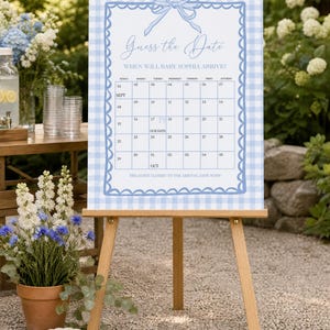 May include: A rectangular Guess the Date sign featuring a light blue and white gingham border with a scalloped edge and a blue bow illustration. The sign includes a calendar grid for September and October, the text Baby Sophia, and instructions.