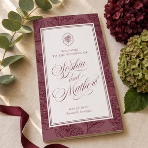 May include: A wedding program with the names "Sophia and Mathew" in elegant script. The program is a deep burgundy color with a floral pattern and the date "May 27, 2029" and location "Roswell, Georgia".