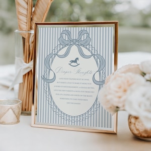 May include: A framed sign with the text "Draper Thoughts" in a decorative font. The sign has a blue and white striped background with a blue bow and rocking horse illustration. The frame is gold.