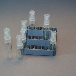 Könnte beinhalten: Ein grauer Plastik-Organizer mit 12 Fächern zum Aufbewahren von kleinen Glasflaschen mit Sprühköpfen. Die Flaschen sind klar und haben einen weißen Plastikverschluss.