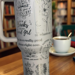 Może przedstawiać: Biały kubek termiczny ze stali nierdzewnej z uchwytem, ​​zawierający różne cytaty i ilustracje w kolorze srebrnym. Kubek zawiera frazy takie jak "Reading is dreaming with your eyes open" i "Buy me books & call me a good girl."