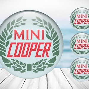 Peut inclure: Trois boutons ronds, blancs et brillants avec un design de laurier vert et le texte "MINI COOPER" en lettres rouges.