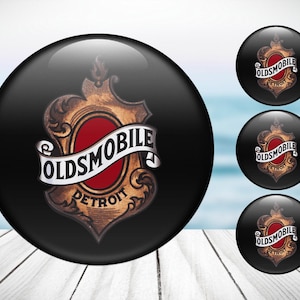 Peut inclure: Quatre boutons ronds noirs et dorés avec le logo Oldsmobile et les mots "Oldsmobile" et "Detroit".