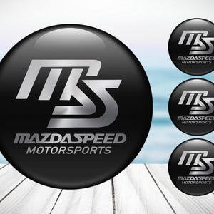 May include: Four black and silver round stickers with the text "MazdaSpeed Motorsports" and the letters "MS" in a stylised font.