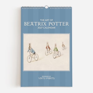 May include: A 2027 wall calendar titled The Art of Beatrix Potter with a blue striped cover. The center features an illustration of four rabbits riding bicycles. The bottom text reads Designed by Vintij Prints in white lettering on a blue background.