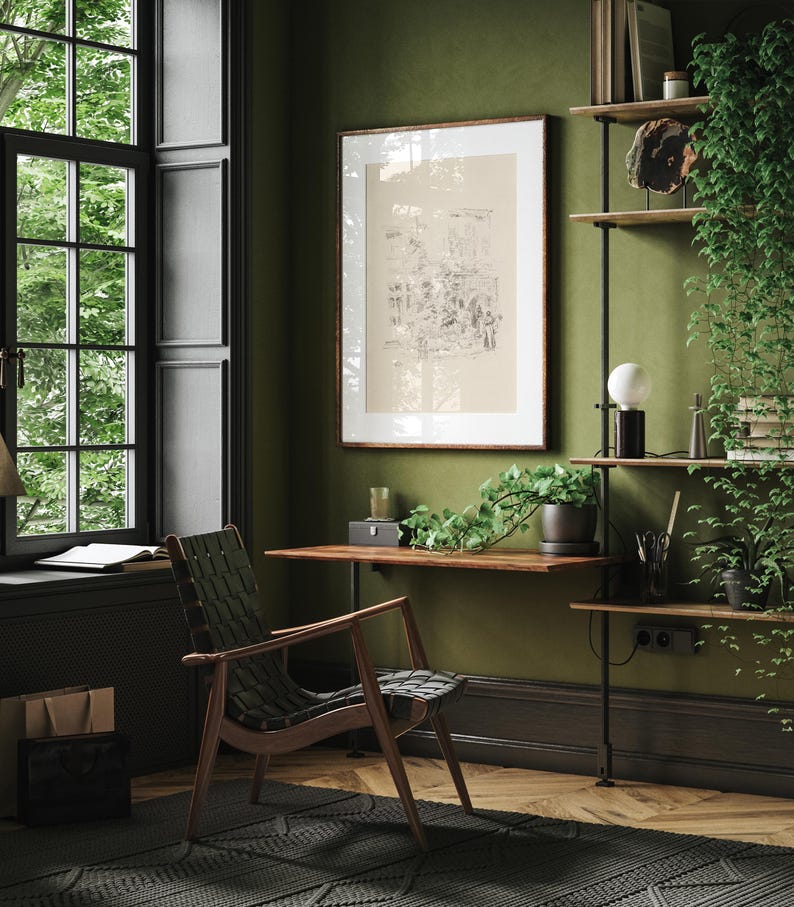 May include: A green room with a wooden desk and a black leather chair. A framed print hangs on the wall above the desk. A shelf with books and plants is on the right side of the image.
