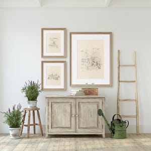 May include: A light wood cabinet with two doors, a wooden ladder, and three framed black and white drawings on a white wall. There are two potted plants with lavender flowers and a green watering can on the floor.